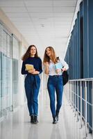 Due giovane donne con libro chat mentre in piedi nel Università corridoio. Università studenti nel corridoio dopo il conferenza. foto