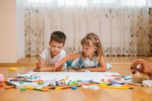 bambini disegno su pavimento su carta. prescolastico ragazzo e ragazza giocare su pavimento con educativo giocattoli - blocchi, treno, Ferrovia, aereo. giocattoli per prescolastico e asilo. bambini a casa o asilo nido foto