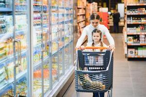 famiglia nel il supermercato. bellissimo giovane mamma e sua poco figlia sorridente e acquisto cibo. il concetto di salutare mangiare. raccogliere foto