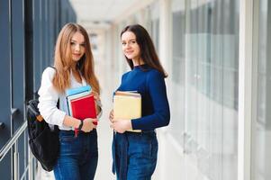 Due femmina studenti In piedi nel il corridoio di il Università con libri foto