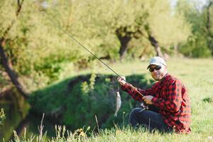 pescatore di il fiume con un' catturare di pesce. uomo pescatore detiene nel mano pesce. foto