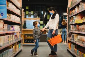 giovane donna e sua poco figlio indossare protettivo viso maschera negozio un' cibo a un' supermercato durante il coronavirus epidemico o influenza scoppio. foto