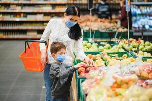 giovane donna e sua poco figlio indossare protettivo viso maschera negozio un' cibo a un' supermercato durante il coronavirus epidemico o influenza scoppio. foto