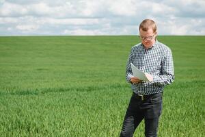 contadino nel rosso verificato camicia utilizzando tavoletta su Grano campo. l'applicazione moderno tecnologia e applicazioni nel agricoltura. concetto di inteligente agricoltura e agroalimentare. foto