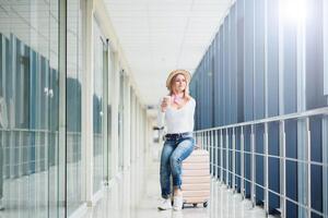 bella ragazza seduta su valigia nel aeroporto terminale. viaggio concetto foto