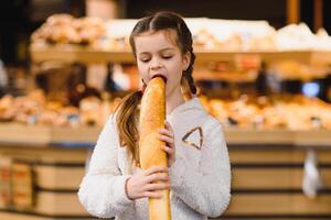 giovane e divertente ragazza mangiare baguettes nel davanti di il forno memorizzare foto