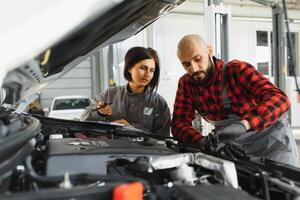 auto servizio, riparazione, Manutenzione e persone concetto - meccanico uomini con chiave inglese riparazione auto motore a laboratorio foto