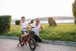 giovane e contento padre insegna il suo giovane figlio per cavalcata un' bicicletta. il bambino è contento . padre Guardando figlio. Il padre di giorno foto