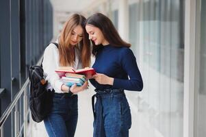 Due giovane femmina studenti in piedi con libri e borse nel il corridoio Università A proposito di ogni Altro. foto
