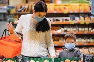 giovane donna e sua poco figlio indossare protettivo viso maschera negozio un' cibo a un' supermercato durante il coronavirus epidemico o influenza scoppio. foto