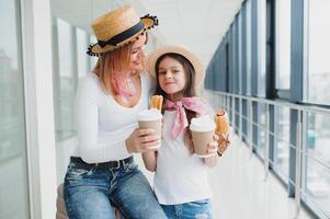 mamma e sua figlia siamo in attesa per un' vacanza in attesa per un' aereo a il aeroporto terminale con bagaglio. in attesa per aereo mamma con figlia mangiare veloce cibo foto