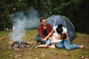 famiglia vicino il fuoco nel il foresta. genitore con bambino su un' tenda sfondo. nazionale parco. escursione con bambini. attivo estate vacanze foto