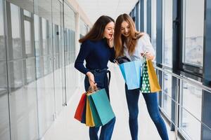 contento Due caucasico donne siamo fare shopping insieme a il centro commerciale centro. Due giovane donne siamo a piedi con shopping borse a centro commerciale. foto