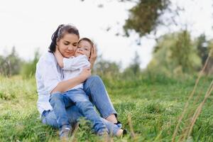 contento giovane madre è giocando con sua bambino nel un' parco su un' verde prato. felicità e armonia di famiglia vita. grande famiglia vacanza. bene fine settimana. madri giorno. vacanza. il concetto di un' contento famiglia foto