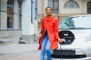 africano americano ragazza ricarica elettro auto a il elettrico gas stazione. foto