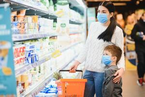giovane donna e sua poco figlio indossare protettivo viso maschera negozio un' cibo a un' supermercato durante il coronavirus epidemico o influenza scoppio. foto