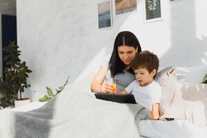 bellissimo sorridente madre e figlio giocando con digitale tavoletta posa su letto. foto