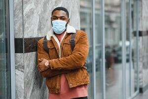 avvicinamento ritratto di un' elegante africano americano tipo sta solo nel il strada nel un' protettivo maschera su il suo viso. precauzionale le misure. foto