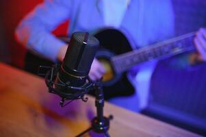 un' giovane elegante tipo con un' barba indossare casuale o musica insegnante giocando chitarra nel davanti di smartphone telecamera. in linea chitarra formazione o vocale lezione foto