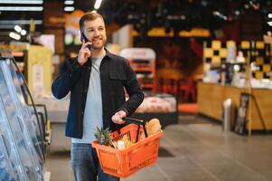 bello uomo acquisto alcuni salutare cibo e bevanda nel moderno supermercato o drogheria negozio. stile di vita e consumismo concetto. foto