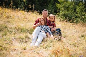 famiglia di tre persone riposo nel il montagne. essi sat giù per riposo, bevanda acqua dopo un' difficile scalata per il montagna. essi siamo stanco ma contento. foto