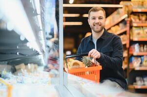 bello uomo acquisto alcuni salutare cibo e bevanda nel moderno supermercato o drogheria negozio. stile di vita e consumismo concetto. foto