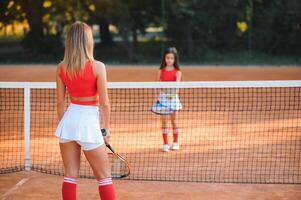 poco ragazza e sua madre giocando tennis su Tribunale foto