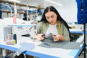 giovane sarta donna cuce Abiti su Lavorando tavolo. sorridente sarta e sua mano vicino su nel officina. foto