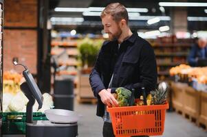 bello uomo acquisto alcuni salutare cibo e bevanda nel moderno supermercato o drogheria negozio. stile di vita e consumismo concetto. foto