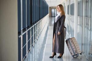 attraente giovane donna con viaggio valigia in piedi su secondo pavimento di aeroporto in attesa camera azione foto