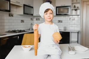 ragazzo nel cucinare cappello seduta a un' cucina contatore. poco ragazzo nel cucina foto