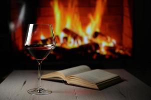 bicchiere di vino rosso secco, libro aperto e caminetto foto