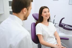 Immagine di bella giovane donna seduta nel dentale sedia a medico centro mentre professionale medico fissaggio sua denti foto