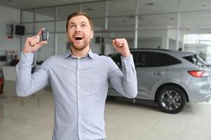 emotivo bello tipo raccolta mano su e sorridente a telecamera. ricco uomo acquisto auto a lusso concessionaria salone foto