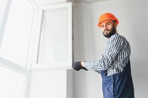 operaio nel tuta da lavoro installazione o regolazione plastica finestre nel il vivente camera a casa foto