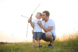 padre è apprendimento il suo figlio per sparare a partire dal arco nel soleggiato estate giorno. foto