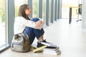 irritato adolescente ragazza sedersi su pavimento purtroppo Guarda su finestra preoccupato di adolescenziale problema a scuola e comunicazione con genitore. preoccupato ragazza teso soffrire di bullismo a scuola foto