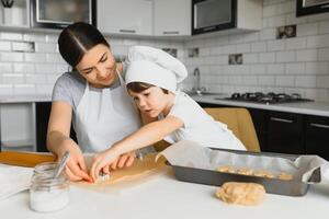 poco ragazzo porzione il suo madre con il cottura al forno nel il cucina in piedi a il contatore a fianco sua impasto il Impasto per il torta foto