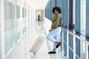 giovane africano americano femmina passanger nel casuale Abiti è nel aeroporto con Bagaglio. foto