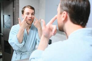 bello giovane uomo l'applicazione crema su il suo viso nel bagno foto