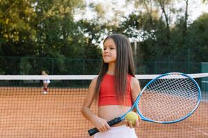 bambino giocando tennis su all'aperto Tribunale. poco ragazza con tennis racchetta e palla nel sport club. attivo esercizio per bambini. estate attività per bambini. formazione per giovane ragazzo. bambino apprendimento per giocare foto