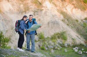 coppia nel amore viaggi nel il montagne con un' carta geografica e binocolo. amici i viaggiatori siamo guardare per indicazioni su il carta geografica. uomo e donna turisti nel il montagne. saltare e rallegrarsi quello essi avere foto