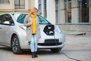 appena aspettare. piacevole carino bionda donna pendente su sua auto ricarica esso e guardare a parte foto