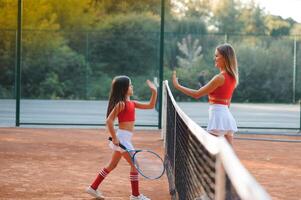 poco ragazza e sua madre giocando tennis su Tribunale foto