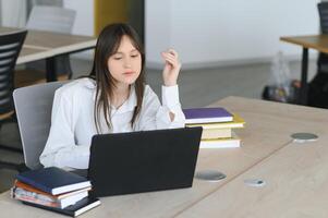 un' bellissimo caucasico femmina alunno è studiando nel Università a distanza. lei è seduta con un' il computer portatile e un' bloc notes e concentrato è Guardando un' video conferenza lezione foto