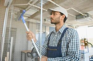 indiano maschio professionale pulizia servizio lavoratore pulisce il finestre e negozio finestre di un' memorizzare con speciale attrezzatura foto