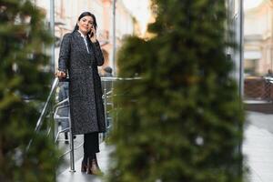 attraente giovane donna nel il città. attività commerciale signora è sorridente mentre parlando su un' inteligente Telefono nel davanti di moderno attività commerciale centro foto