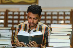 maschio indiano alunno a il biblioteca con libro foto
