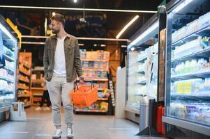 giovane uomo acquisto drogheria a il supermercato. altro i clienti nel sfondo. consumismo concetto. foto