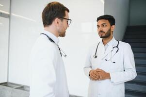 un indiano medico e un' europeo medico In piedi insieme nel un' ospedale atrio. foto
